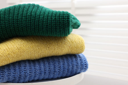 Stack of woolen sweaters on table near window, closeup