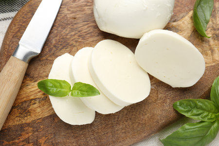 Cut mozzarella cheese with basil and knife on wooden table, flat layの写真素材
