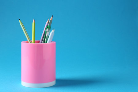 Pencils and pens in holder on light blue backgroundの写真素材