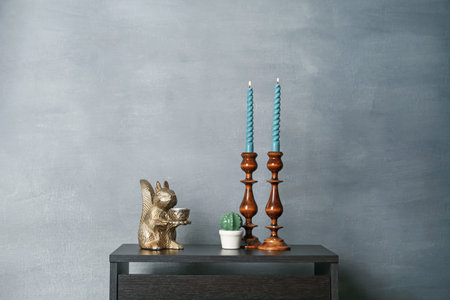 Elegant candlesticks with burning candles and other decor on black wooden table near grey wall