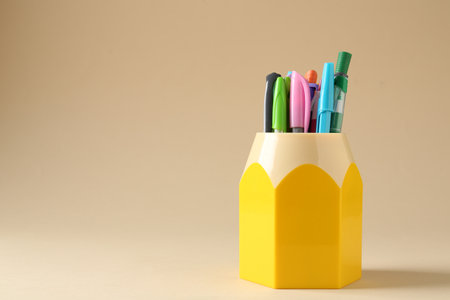 Pencils and pens in holder on beige background. Space for textの写真素材