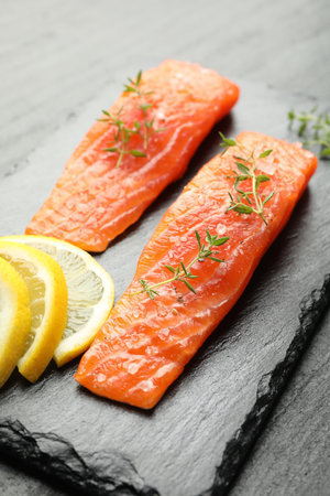 Seafood. Pieces of salmon fillet, thyme and lemon slices on black table, closeupの写真素材