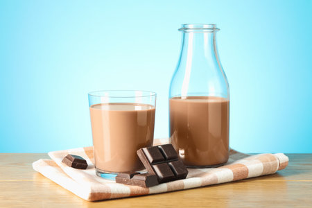 Tasty chocolate milk in glass, bottle and pieces on wooden table against light blue backgroundの写真素材