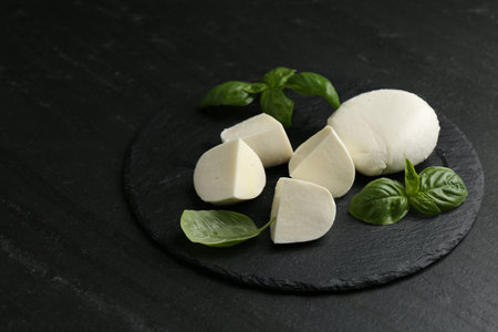Pieces of delicious mozzarella cheese and basil on dark textured table, closeupの写真素材