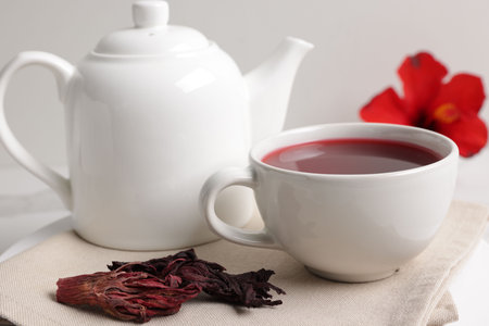 Delicious hibiscus tea in cup, teapot and dry roselle sepals on white table, closeupの写真素材