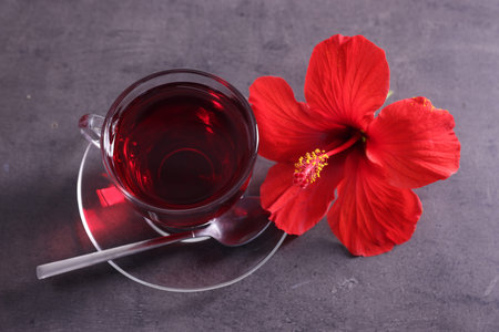 Tasty hibiscus tea in cup and beautiful flower on grey textured table, closeupの写真素材