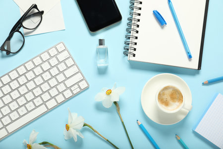 Flat lay composition with stationery, coffee and flowers on light blue background