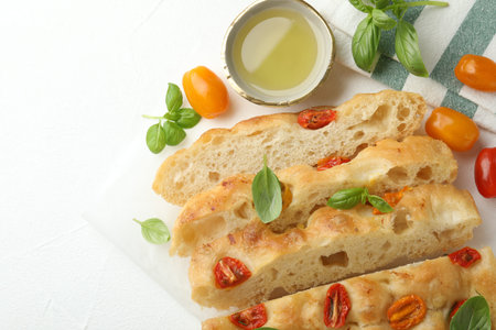 Cut delicious focaccia with tomatoes, basil and oil on light table, flat lay. Space for text