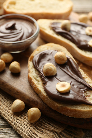 Slices of bread with chocolate spread and hazelnuts on wooden table, closeupの写真素材