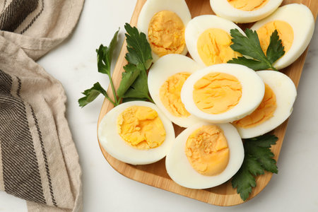 Boiled eggs and parsley on white marble table, top view