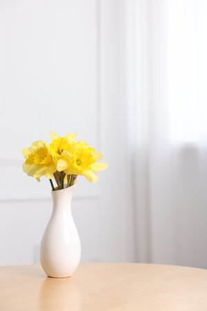 Beautiful daffodils in vase on wooden table at home. Space for textの写真素材