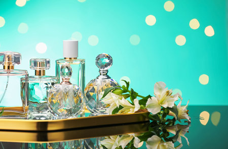 Many different perfume bottles and flowers on mirror surface against turquoise background with...