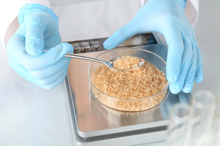 Scientist weighing Petri dish with sample on scales at white mirror table, closeupの写真素材