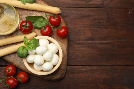 Tasty mozzarella cheese balls, breadsticks, tomatoes and basil on wooden table, flat lay. Space for textの写真素材