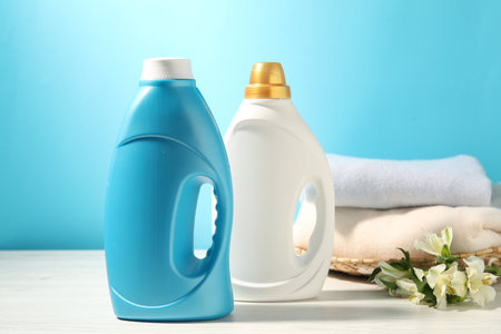 Bottles of fabric softener, clean clothes and lily flowers on white wooden table against light blue backgroundの写真素材