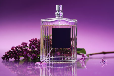 Bottle of perfume and branch with lilac flowers on mirror surface against color gradient background, closeupの写真素材