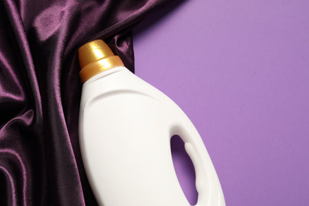 Bottle of fabric softener and color cloth on purple background, top view. Space for textの写真素材