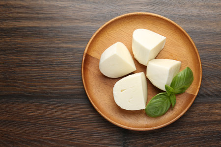 Pieces of delicious mozzarella cheese and basil on wooden table, top view. Space for textの写真素材