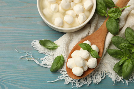 Mozzarella cheese balls and basil on blue wooden table, flat lay