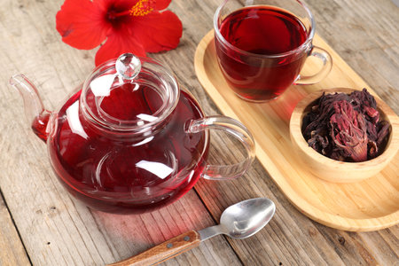 Delicious hibiscus tea in glass cup, teapot, dry roselle sepals and flower on wooden table, closeupの写真素材