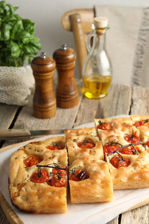 Cut delicious focaccia with tomatoes, spices and oil on wooden table indoorsの写真素材