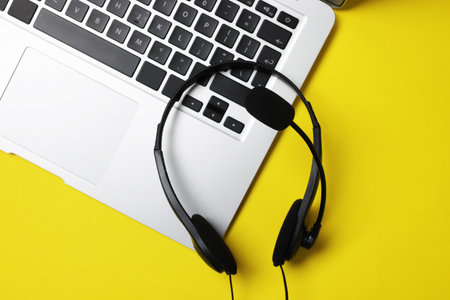 Headset with microphone and laptop on yellow background, top viewの写真素材