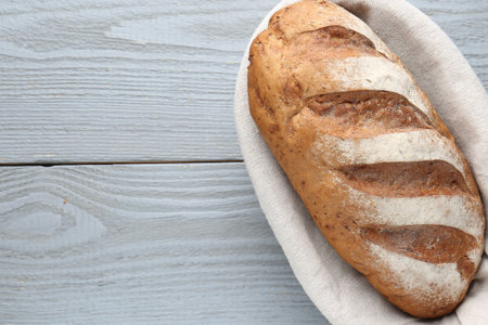 Loaf of bread in basket on grey wooden table, top view. Space for text