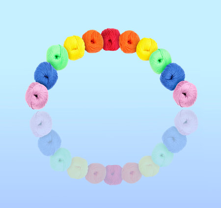 Rainbow arch made of knitting thread in different colors on light blue background with reflection