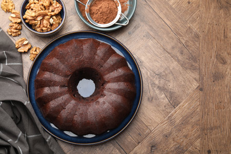 Tasty chocolate bundt cake, walnuts and cocoa powder on wooden table, flat lay. Space for textの写真素材