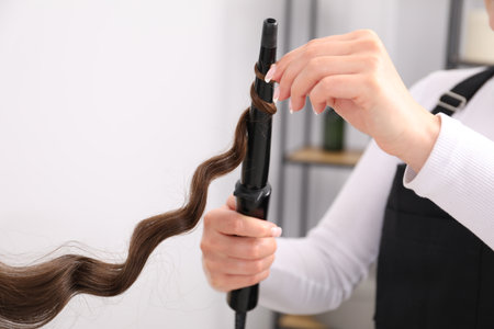 Hairdresser curling woman's hair in salon, closeup. Space for textの写真素材