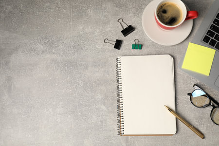 Notebook, pen, sticky note, binder clips, glasses, coffee and laptop on grey table, flat lay. Space for textの写真素材