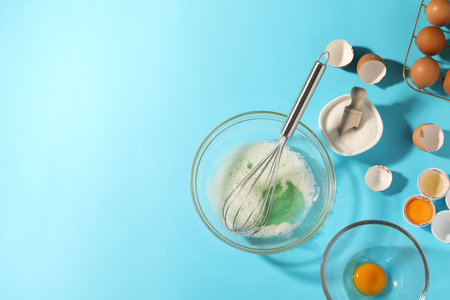 Egg whites in bowl, whisk, sugar and eggs on light blue table, flat lay. Space for textの写真素材