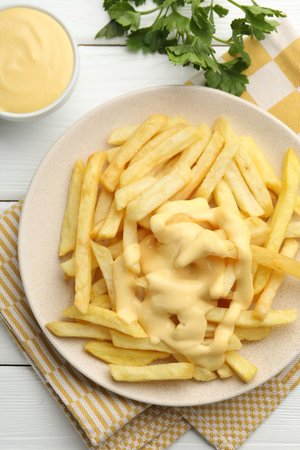 French fries with cheese sauce and parsley on white wooden table, flat lay