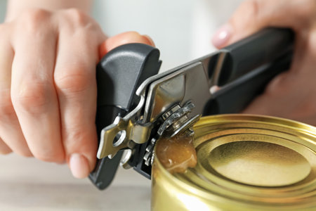 Woman opening tin with can opener at white table, closeupの写真素材
