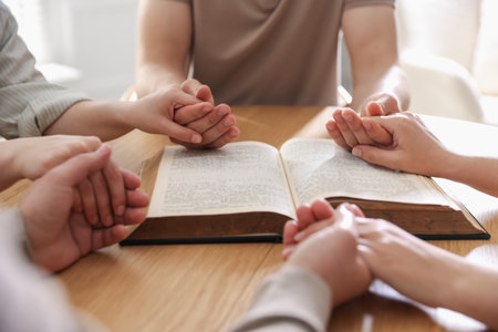 Family with Bible praying at wooden table indoors, closeupの写真素材