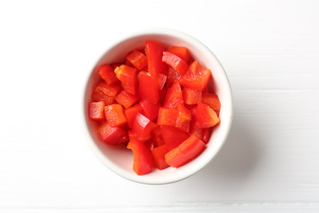 Pieces of fresh red bell pepper in bowl on white wooden table, top viewの写真素材