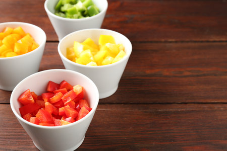 Pieces of fresh colorful bell peppers in bowls on wooden table, closeup. Space for textの写真素材