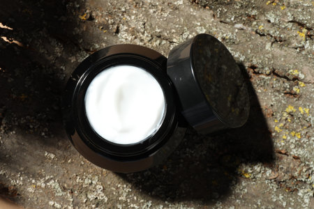 Jar of body cream on tree bark, top view