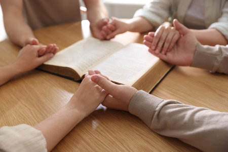 Family with Bible praying at wooden table indoors, closeupの写真素材