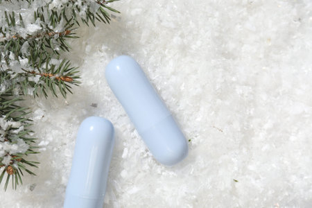 Moisturizing lip balms and fir tree branches on artificial snow, flat lay. Space for text