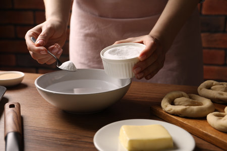 Making pretzels. Woman adding baking soda into bowl of water at wooden table, closeupの写真素材