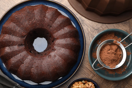 Tasty chocolate bundt cake, walnuts and cocoa powder on wooden table, flat layの写真素材