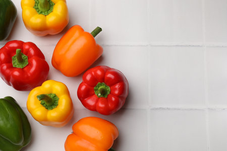 Fresh colorful bell peppers on white tiled table, flat lay. Space for textの写真素材