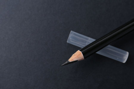 Black eyebrow pencil on dark background, top view. Space for textの写真素材
