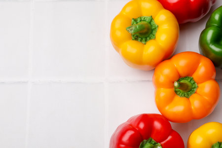 Fresh colorful bell peppers on white tiled table, flat lay. Space for textの写真素材