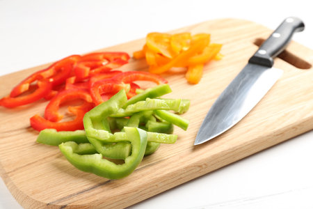 Slices of fresh colorful bell peppers and knife on white wooden table, closeupの写真素材