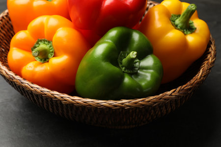 Fresh colorful bell peppers in wicker basket on dark table, closeupの写真素材