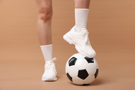 Woman in sneakers with soccer ball on beige background, closeupの写真素材