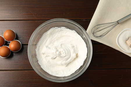 Bowl with whipped cream, whisk and ingredients on wooden table, flat layの写真素材
