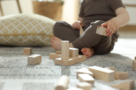 Cute little child playing with wooden building blocks at home, closeup. Space for textの写真素材